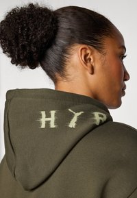 Moleton verde-oliva com uma textura suave, apresentando um grande gráfico desgastado "HYR" em verde claro nas costas, com design de capuz.