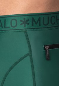 Zöld férfi boxeralsó, fekete derékrésszel, amelyen a "MUCHO" felirat látható, valamint egy kis cipzáros zseb. Sima, rugalmas szövet, megerősített varratokkal.