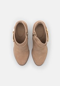 Botines de ante beige con punta afilada, cremallera lateral y detalles en dorado. Textura suave con un pequeño tacón elevado.