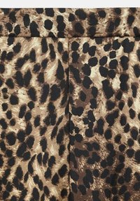 Tejido con estampado de leopardo que presenta una combinación de colores marrón claro y negro, con una superficie texturizada y manchas irregulares de diferentes tamaños.