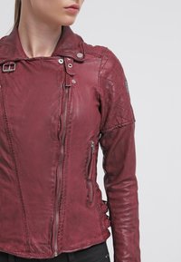 Bordeauxrode leren jas met een gewatteerd schouderontwerp, ritszakken en een kraag met riem, met een gladde textuur en een aansluitende pasvorm.