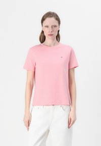 T-shirt in cotone rosa chiaro con scollatura rotonda e maniche corte. Presenta un piccolo logo sul petto. Abbinato a pantaloni bianchi.