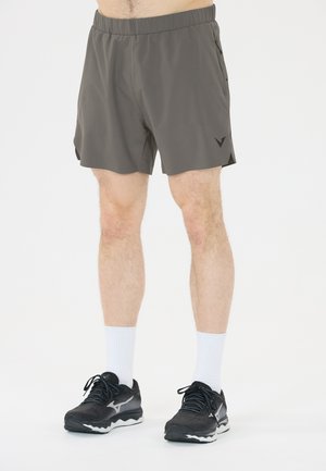 Male wearing gray athletic shorts, white crew socks, and black running shoes standing on a light background.