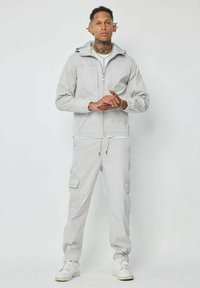 Veste grise clair avec fermeture à glissière et poignets élastiques, accompagnée d'un pantalon cargo assorti avec poches latérales et taille à cordon. Baskets blanches.