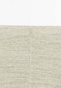 Gros plan d’un tissu tricoté beige montrant une couture verticale et un motif de points texturés.