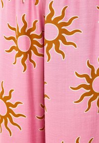 Tissu rose avec de grands motifs de soleil en brun avec des contours blancs. La texture semble lisse et légère, adaptée aux temps chauds.