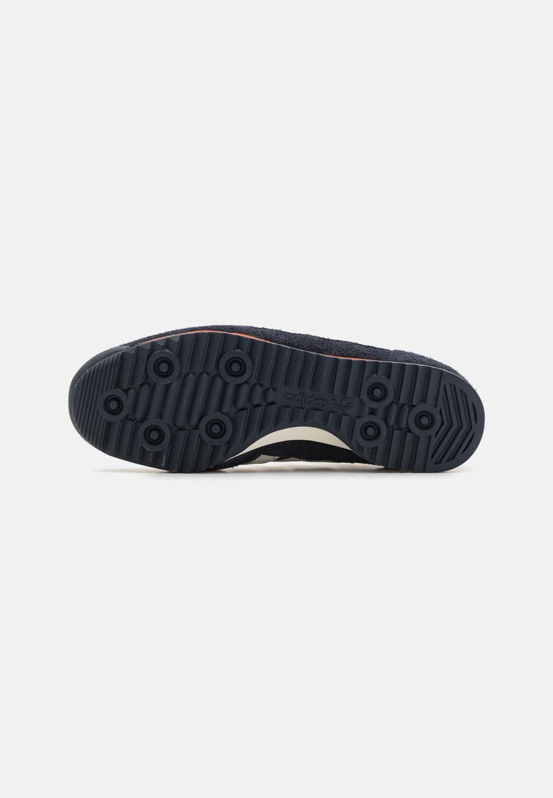 Suela de zapato de goma negra con superficie texturizada, agarres circulares y una franja horizontal. El material parece resistente y está diseñado para ofrecer tracción.