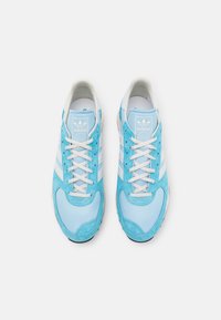 Vaaleansinsiset mokkakengät, joissa on valkoiset raidat ja nauhat. Pyöristetty kärki ja teksturoitu päällinen. Valkoinen logo kielekkeessä, kumipohja.