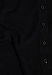 Cardigan en tricot noir avec un devant boutonné, comportant cinq boutons noirs et une texture lisse. Le tissu semble douillet et léger.