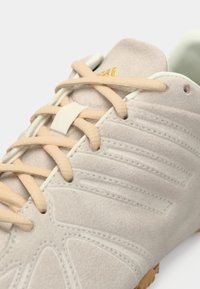 Αθλητικό παπούτσι ανοιχτό μπεζ με υφή από σουέντ, εκρού λεπτομέρειες, κορδόνια ροδακινί και χρυσή λεπτομέρεια λογότυπου στη γλώσσα.