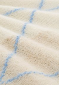 Tissu tricoté de couleur crème avec une texture douce, présentant des lignes bleu clair entrecroisées formant un motif de grille.