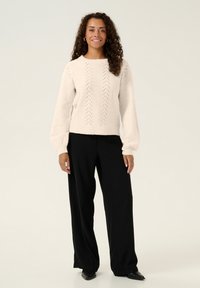 Krämbelagd, stickad tröja med ett zickzacksmönster, ballongärmar och lös passform, ihopparad med svarta vida byxor och svarta skor.