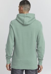 Mintgroene hoodie met een grote capuchon, lange mouwen en geribde manchetten, met een soepel textuur en een kangoeroezak aan de voorkant.