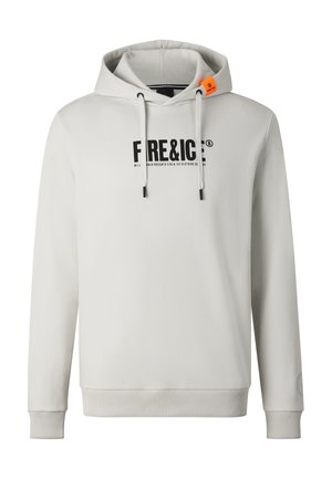 Junger Mann trägt weißen Free & Ice Hoodie, passende Jogginghose, klobige weiße Sneakers und große dunkle Sonnenbrille, steht vor weißem Hintergrund.