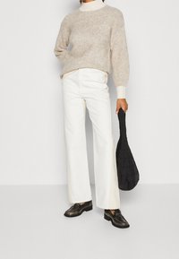 Beiger Strickpullover, cremefarbener Kragen, weiße weite Hosen und schwarze strukturierte Handtasche. Braune Slipper mit metallischem Finish.