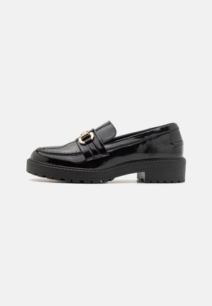 Sorte loafers i laklæder med en guldfarvet spænde, der har en kraftig gummisål og detaljerede syninger langs siderne.