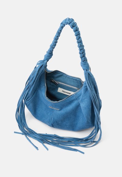Blauwe corduroy handtas met een gevlochten hengsel, voorzien van een ritssluiting en lange franjes langs de zijkanten. De binnenkant is gevoerd met blauwe stof.
