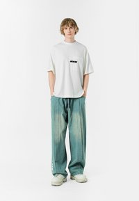 Camiseta blanca oversize con un logo negro en el pecho, combinada con pantalones de mezclilla ligeros y sueltos de color azul y zapatillas chunky beige.