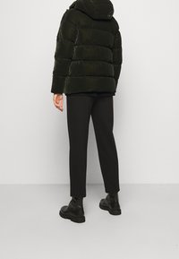 Tmavě zelená prošívaná bunda s kapucí, která má prošívané části. V kombinaci s černými tapered kalhotami a černými vojenskými botami.