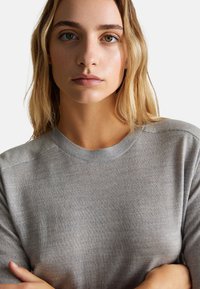 Szary sweter z krótkim rękawem i prążkowanym okrągłym dekoltem. Miękka tekstura, smukły krój i bezszwowe ramiona tworzą gładką sylwetkę.