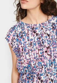 Top a maniche corte con un motivo astratto colorato nelle tonalità di rosa, blu e nero su sfondo bianco; tessuto leggero.