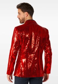 Roter Paillettenblazer mit tailliertem Schnitt, Reverskragen und langen Ärmeln, dessen glatte Textur das Licht reflektiert.