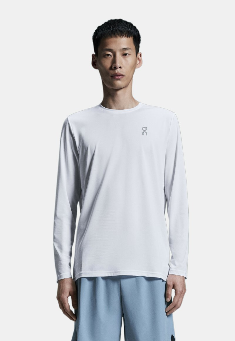 Langærmet hvid sports-t-shirt lavet af let materiale, med rund hals og et lille gråt logo på brystet.