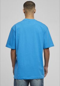Tricou cu mânecă scurtă din bumbac de culoare albastru strălucitor, cu guler la baza gâtului și o croială lejeră, având o textură fină și detalii de coasere minime.
