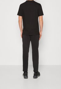 Camiseta negra de manga corta y pantalones a juego. La tela es suave, con un ajuste cómodo. Los zapatos son negros con detalles reflectantes.