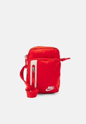 Sac bandoulière rouge Nike avec poche zippée à l'avant, sangle réglable et logo blanc sur le devant sur fond blanc.
