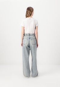 Light blue, wide-leg denim jeans with a high waistband, back pockets, and a slightly faded texture. Paired with a plain white T-shirt.