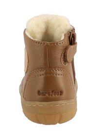 Stivale alla caviglia in pelle marrone con una morbida fodera beige, cerniera laterale e cinturino in Velcro. La scritta "barefoot" è impressa sul retro e la suola in gomma traslucida.