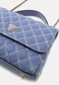 Niebieska pikowana torebka wykonana z teksturowanej syntetycznej skóry. Z białym przeszyciem, złotymi okuciami oraz trójkątnym logo na przedniej części.