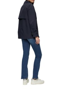 Veste légère bleu marine avec un rabat au dos, poignets à boutons, associée à un jean bleu et des baskets blanches avec des accents argentés.