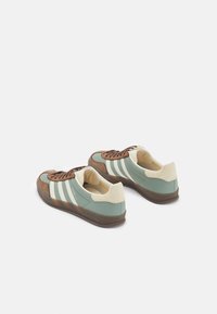 Sportovní boty s designem v mátově zelené a hnědé barvě, vyrobené z nubuku a kůže, tři bílé pruhy a gumová podrážka.