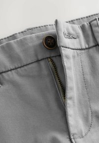 Pantalons en coton gris avec fermeture à glissière en laiton et bouton, dotés de coutures décoratives et d'une surface légèrement texturée pour plus de durabilité.