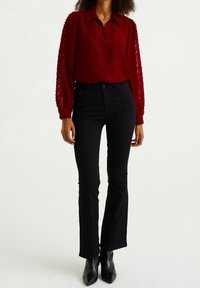 Rote, strukturierte Bluse mit knöpfbarem Design und langen Ärmeln, kombiniert mit schwarzen, engen Jeans und schwarzen Knöchelstiefeln.