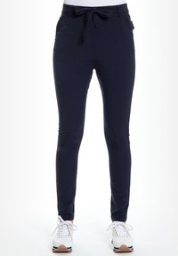 Marineblauwe broek met een aansluitend ontwerp, een trekkoord in de taille en een gladde textuur. Gecombineerd met witte sneakers met gekleurde accenten.