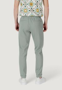 Joggers a gamba affusolata di colore verde chiaro realizzati in tessuto liscio, dotati di una cintura elasticizzata, tasche posteriori e risvolti. Indossati con una camicia a fantasia.