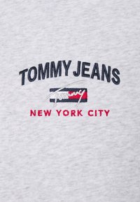 Šedá bavlněná mikina s vyšitým textem v námořnické modré a červené barvě: "TOMMY JEANS" nad "NEW YORK CITY." Detaily zahrnují podpisovou grafiku.