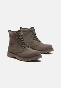 Stivali alla caviglia in pelle marrone con colletto imbottito, punta rotonda, sei asole metalliche e suola in gomma resistente. Logo Timberland sul lato.