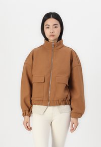 Veste brune zippée avec un col haut, deux poches avant, un ourlet élastiqué et des manches surdimensionnées, fabriquée en tissu doux.