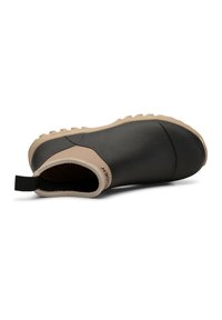 Chaussure en caoutchouc noire avec un accent beige sur le talon et une semelle texturée ; elle dispose d'une languette pour un enfilage facile et d'un design fermé.
