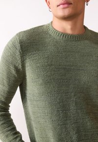 Green knit sweater with a round neckline. Material has a textured finish. Fitted long sleeves and a subtle pattern throughout.