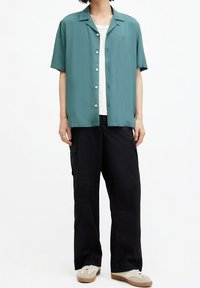 Korte mouw teal shirt met een knoopsluiting, gecombineerd met losse zwarte cargobroeken en beige sneakers, met een textuur stof en zakken.