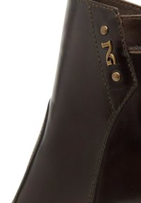 Stivale in pelle marrone scuro con pannelli cuciti e due rivetti in ottone vicino a un piccolo logo metallico sulla parte superiore.