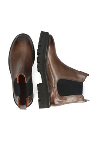 Botas Chelsea de cuero marrón con paneles laterales elásticos, una suela de goma negra texturizada y acentos naranjas en la apertura del tobillo.