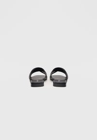 Czarne, płaskie sandały z dwoma szerokimi paskami i teksturowanym wykończeniem. Podeszwa jest gładka i płaska, zapewniając komfort. Minimalistyczny design o nowoczesnym wyglądzie.