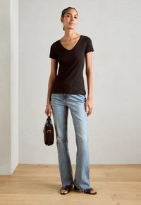 Black short-sleeve V-neck t-shirt, faded blue flared jeans, brown handbag with a handle, and black slip-on sandals on wooden floor.