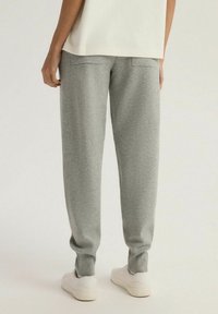 Szare dresowe spodnie z miękkiego materiału, o luźnym kroju, z elastycznymi mankietami i tylnymi kieszeniami. Stylizowane z białymi trampkami.